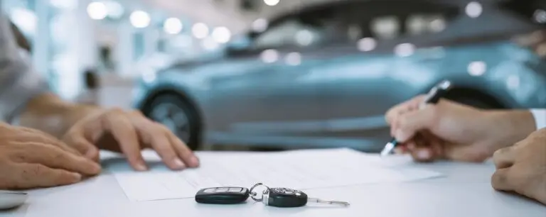 Hands signing a car leasing contract with the keys on the table