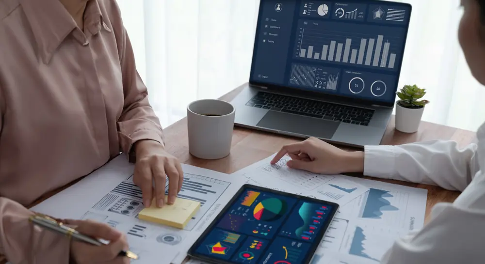 Finance team reviewing reports and a dashboard on a laptop and tablet
